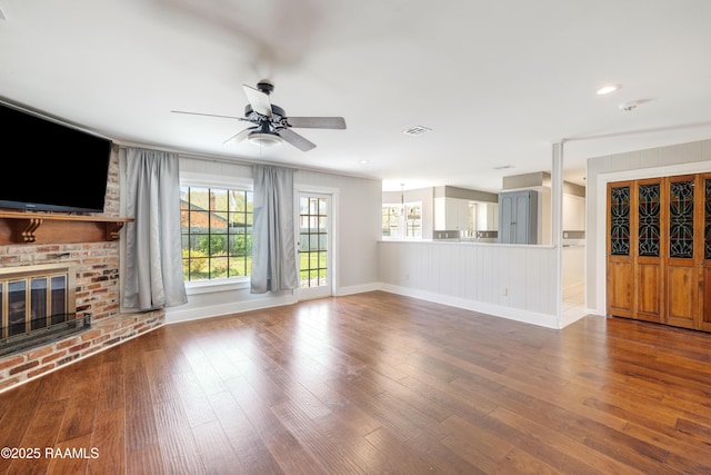 unfurnished living room with a ceiling fan, a brick fireplace, wood finished floors, and visible vents