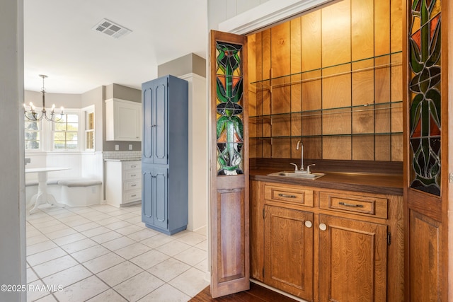 kitchen with visible vents, light tile patterned flooring, a sink, dark countertops, and brown cabinets