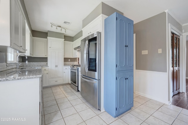 kitchen featuring light tile patterned floors, stainless steel appliances, light stone counters, and a sink