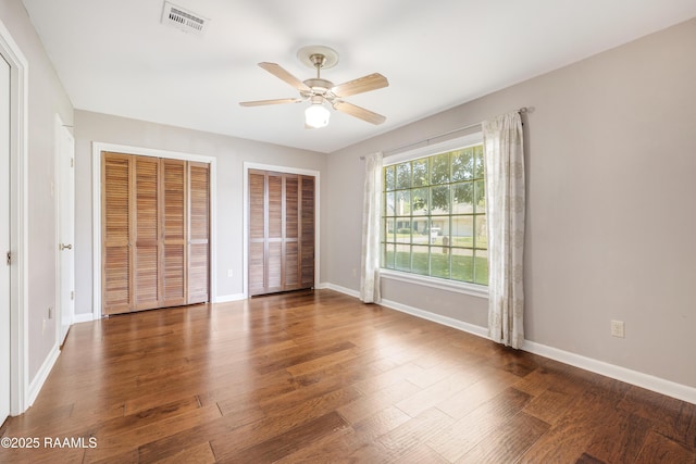 unfurnished bedroom with visible vents, baseboards, multiple closets, and wood finished floors