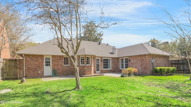 rear view of property with brick siding, a shingled roof, fence, a lawn, and a patio area