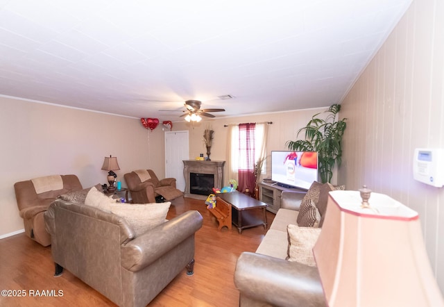 living area featuring ornamental molding, a glass covered fireplace, a ceiling fan, and light wood-style floors