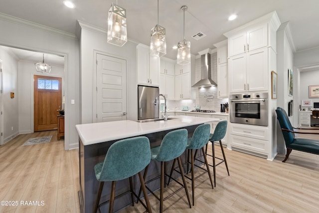 kitchen with light countertops, wall chimney range hood, appliances with stainless steel finishes, and white cabinets