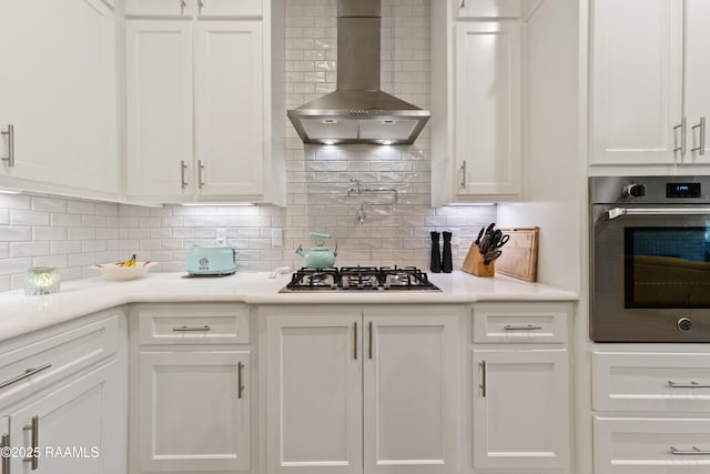 kitchen featuring wall chimney exhaust hood, light countertops, stainless steel oven, and white cabinetry