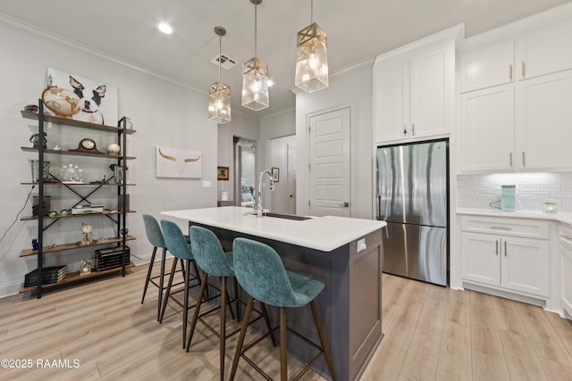 kitchen with a sink, white cabinetry, light countertops, freestanding refrigerator, and a center island with sink