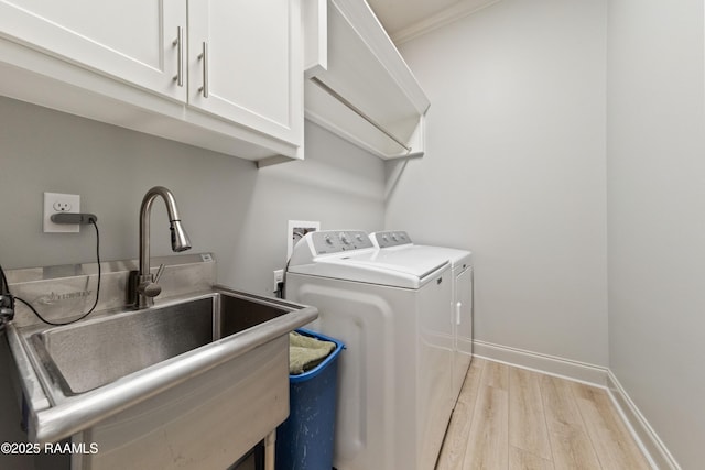 laundry area featuring cabinet space, baseboards, light wood-style flooring, washing machine and clothes dryer, and a sink