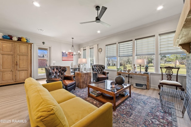 living area featuring light wood-style floors, recessed lighting, ornamental molding, and ceiling fan with notable chandelier