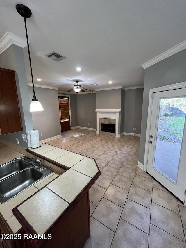 kitchen with visible vents, a tile fireplace, tile countertops, crown molding, and a sink