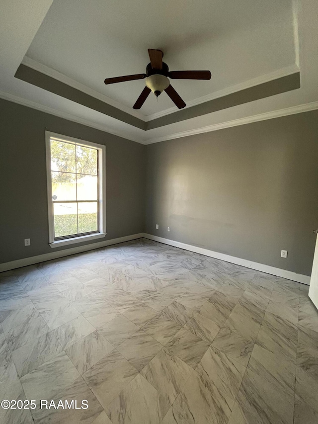 spare room with ornamental molding, a tray ceiling, and baseboards