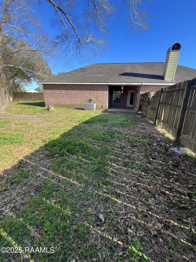 back of house with a fenced backyard, central air condition unit, brick siding, a yard, and roof with shingles