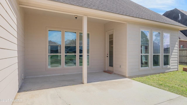 property entrance featuring a patio, roof with shingles, and fence