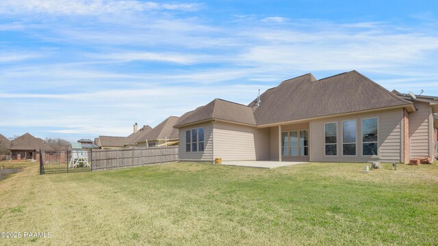 rear view of property with a yard, fence, a shingled roof, and a patio