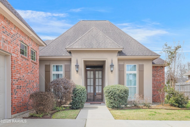 view of exterior entry featuring stucco siding, a shingled roof, brick siding, and french doors