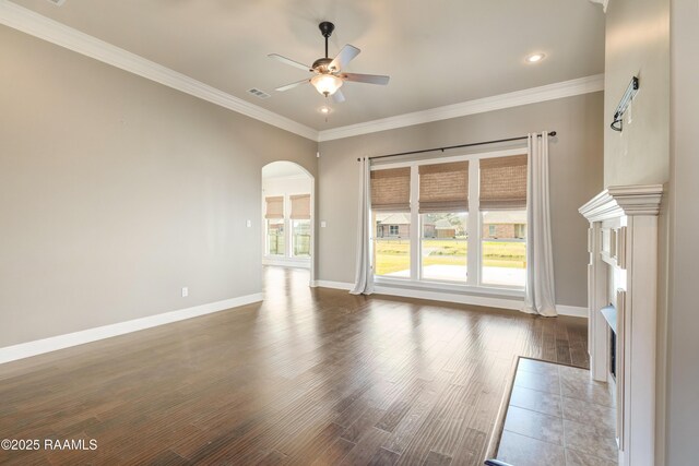 unfurnished living room featuring arched walkways, wood finished floors, a ceiling fan, baseboards, and ornamental molding