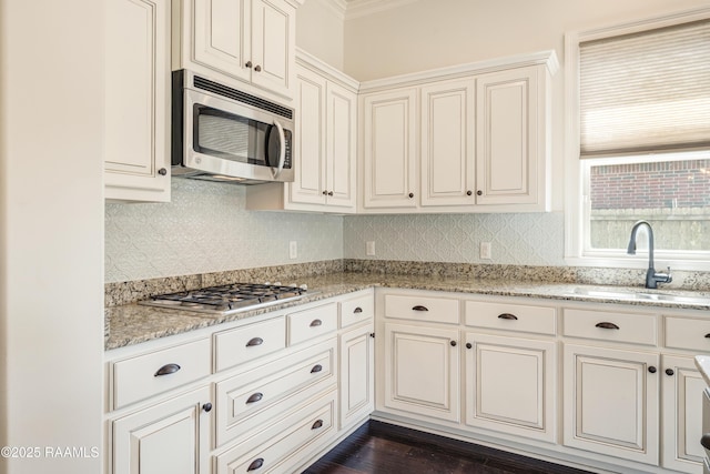 kitchen with light stone counters, backsplash, appliances with stainless steel finishes, ornamental molding, and a sink