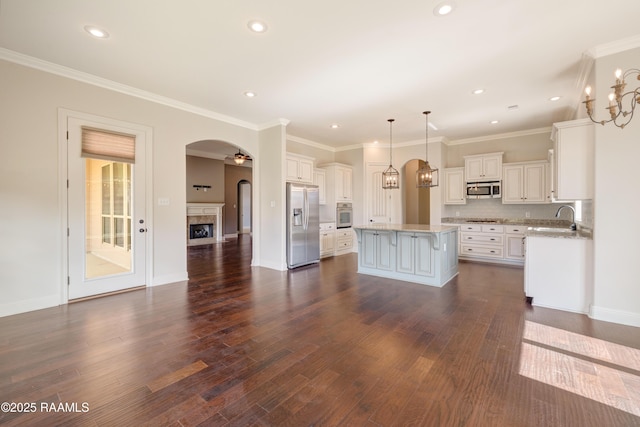 kitchen featuring arched walkways, dark wood-style flooring, a center island, stainless steel appliances, and a fireplace