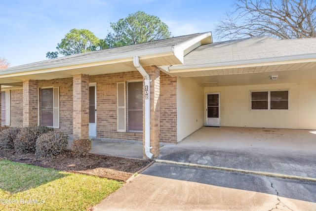 doorway to property with driveway, a carport, and brick siding