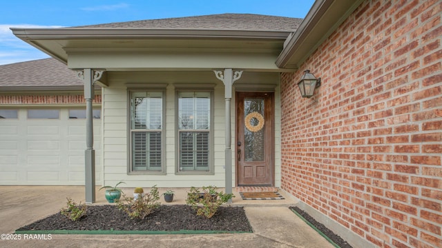 entrance to property featuring a garage, concrete driveway, brick siding, and roof with shingles