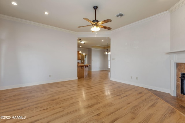 unfurnished living room with visible vents, a tiled fireplace, light wood-style floors, ornamental molding, and ceiling fan with notable chandelier