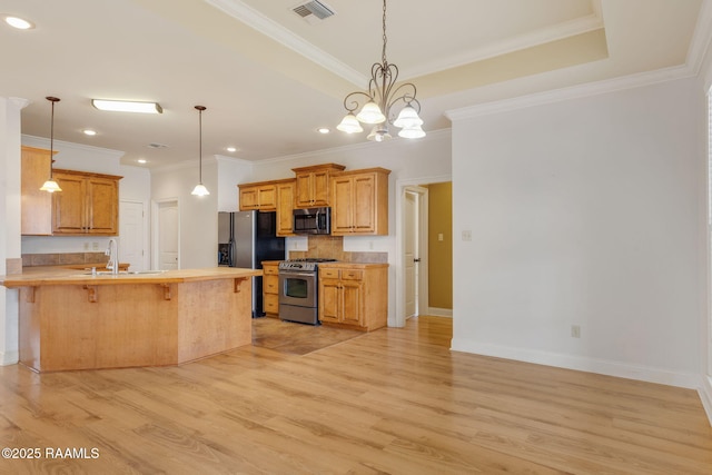 kitchen featuring visible vents, appliances with stainless steel finishes, a tray ceiling, light wood finished floors, and a kitchen bar