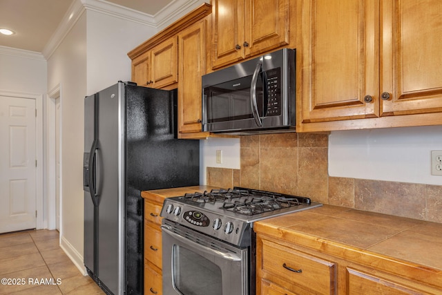 kitchen featuring tile counters, decorative backsplash, ornamental molding, stainless steel appliances, and light tile patterned flooring