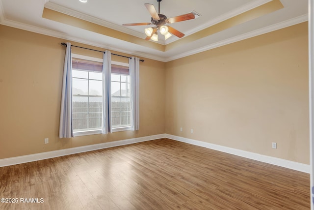 empty room featuring baseboards, a tray ceiling, wood finished floors, and ornamental molding