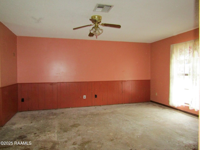 unfurnished room with a wainscoted wall, visible vents, a ceiling fan, wood walls, and concrete floors