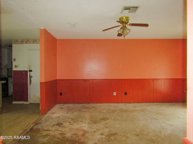 unfurnished room with ceiling fan, wood walls, visible vents, wainscoting, and unfinished concrete floors