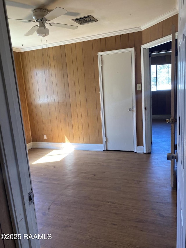 spare room featuring ceiling fan, wood walls, wood finished floors, visible vents, and crown molding