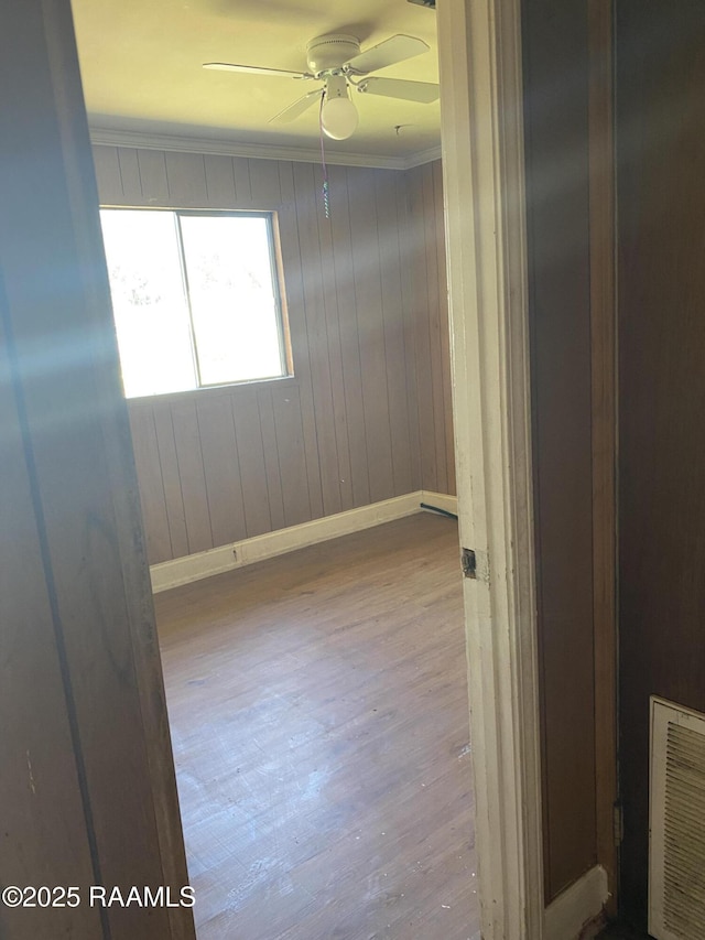 empty room featuring baseboards, visible vents, a ceiling fan, wood finished floors, and crown molding