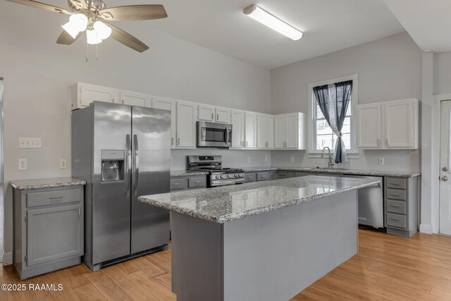 kitchen featuring a sink, a center island, light wood-style floors, appliances with stainless steel finishes, and light stone countertops