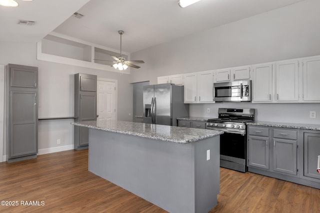 kitchen featuring gray cabinetry, a center island, dark wood-type flooring, light stone countertops, and appliances with stainless steel finishes