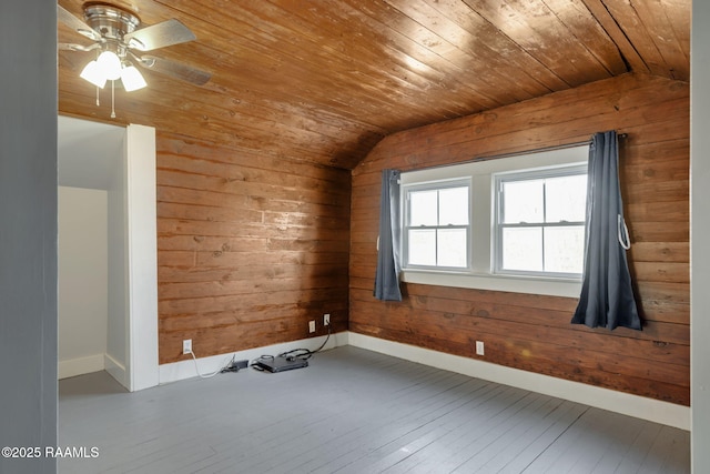 empty room featuring baseboards, wood walls, lofted ceiling, wooden ceiling, and wood-type flooring