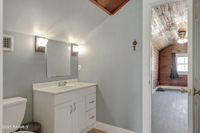 half bath with toilet, lofted ceiling, wood finished floors, baseboards, and vanity