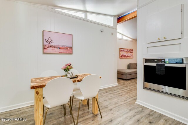 dining space featuring vaulted ceiling with beams, light wood-style flooring, and baseboards