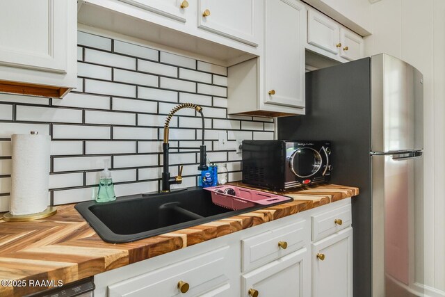 kitchen with dishwashing machine, a sink, wood counters, white cabinetry, and backsplash