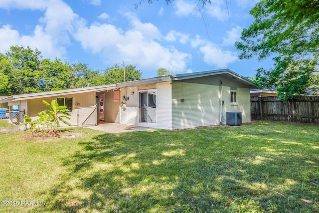 back of house featuring brick siding, fence, central AC, and a yard