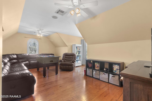 living area with a ceiling fan, visible vents, vaulted ceiling, and wood finished floors