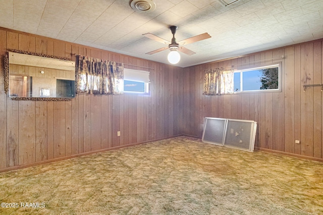 carpeted spare room with wood walls, plenty of natural light, baseboards, and ceiling fan