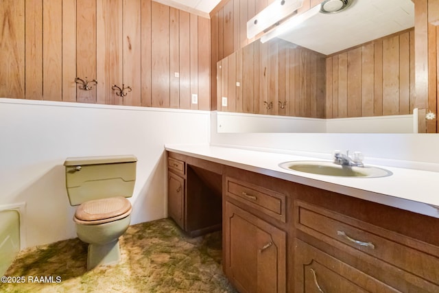 bathroom with toilet, wood walls, and vanity