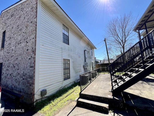 view of side of property featuring brick siding, fence, and stairs