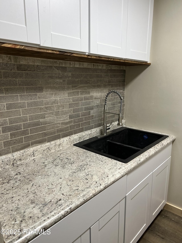 kitchen with backsplash, dark wood-type flooring, white cabinetry, a sink, and light stone countertops