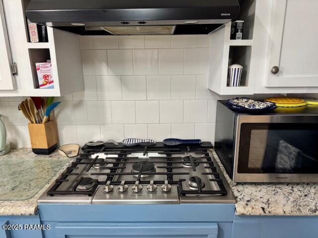 interior details with white cabinets, under cabinet range hood, stainless steel appliances, and backsplash