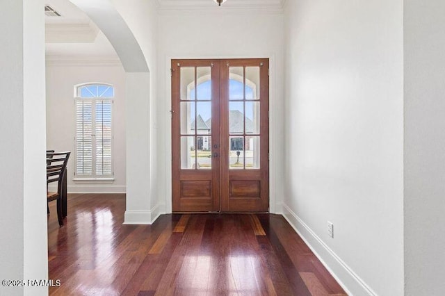 foyer entrance with arched walkways, dark wood-type flooring, visible vents, baseboards, and ornamental molding