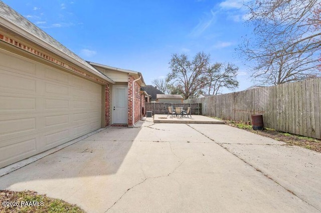 view of side of property featuring outdoor dining space, fence, concrete driveway, and brick siding