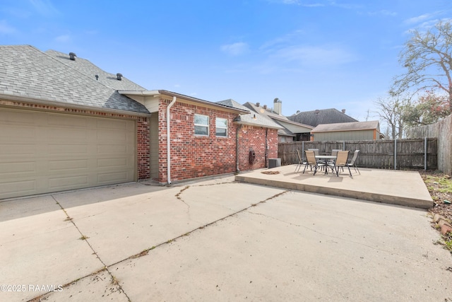 back of house with a garage, brick siding, a shingled roof, fence, and a patio area