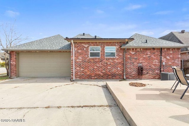 exterior space featuring driveway, an attached garage, a shingled roof, and brick siding