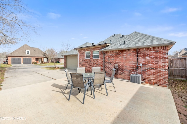 view of patio with central AC unit, outdoor dining space, fence, a garage, and driveway