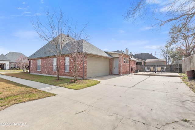 view of property exterior with an attached garage, brick siding, fence, concrete driveway, and a lawn