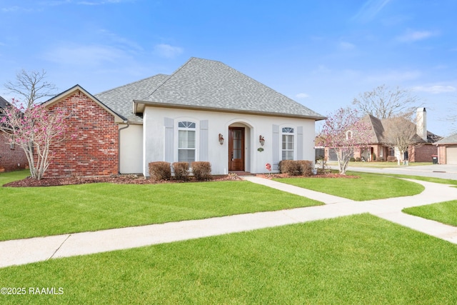 view of front of property featuring a shingled roof, brick siding, a front lawn, and stucco siding